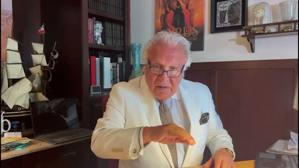 A man sitting in his office wearing a white suit